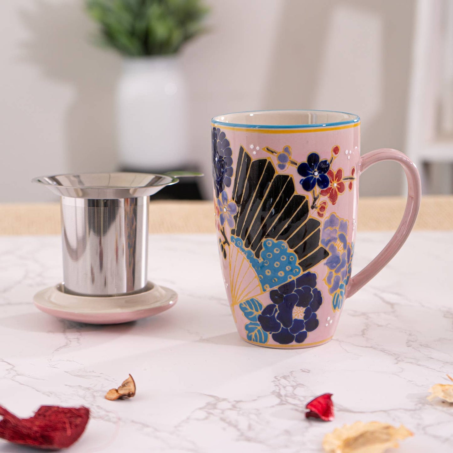 Decorative mug with floral design next to a metal tea filter on a light surface.