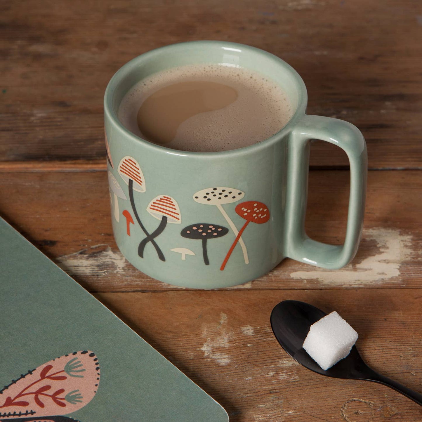 Green mug with mushroom design filled with a hot beverage on a wooden surface.