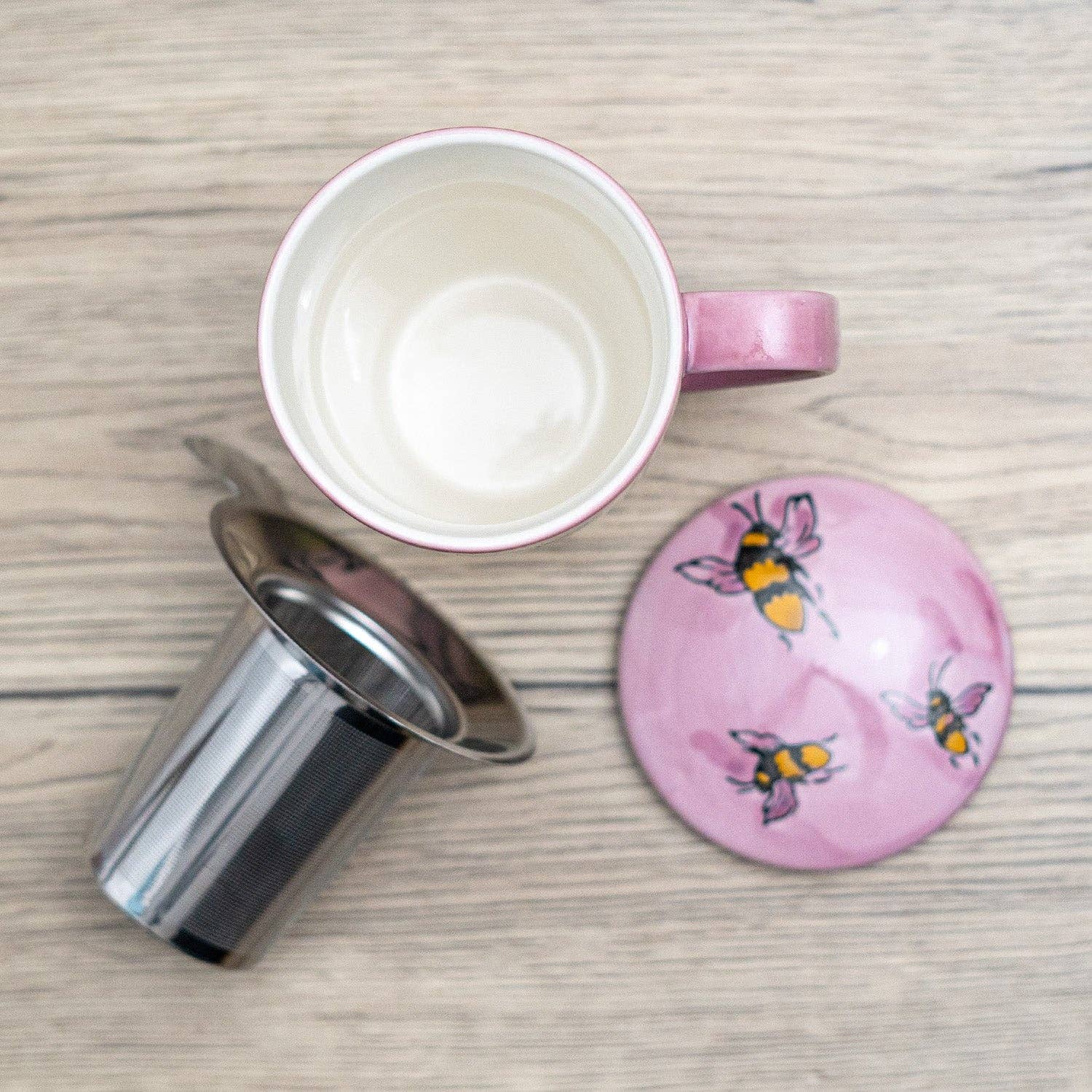 Pink mug with a metal lid and pink coaster with bee design on a wooden surface