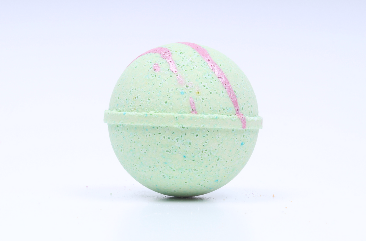 A spherical bath bomb with a speckled mint green texture, decorated with pink swirls and tiny multicolored glitter, shown on a clean white background.