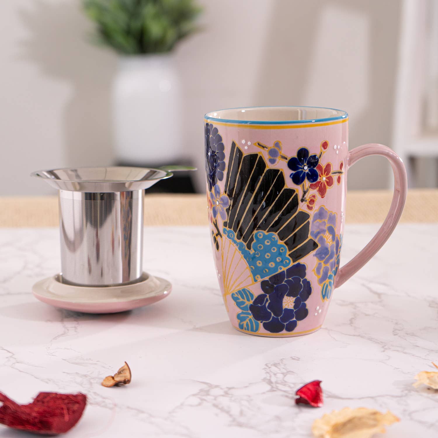 Decorative mug with floral design next to a metal tea filter on a light surface.