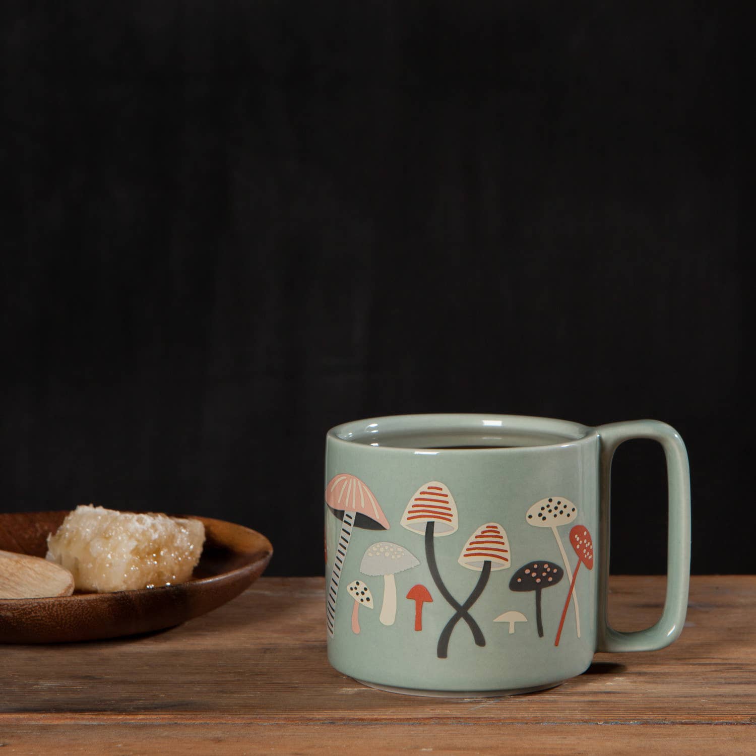 Green mug with mushroom design on a wooden table with a dark background