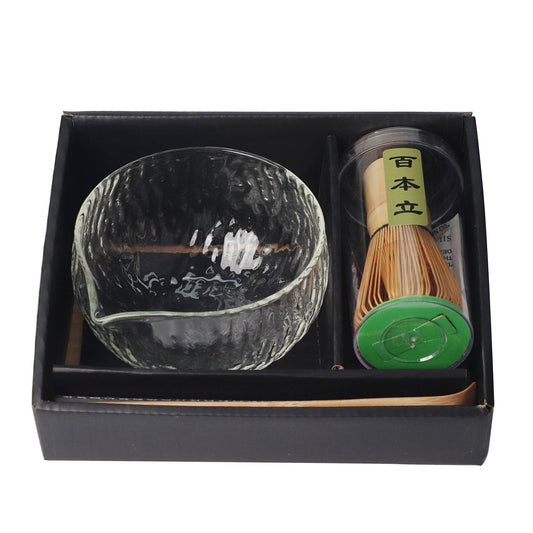 Tea set with a glass bowl, whisk, and container in a black box on a white background