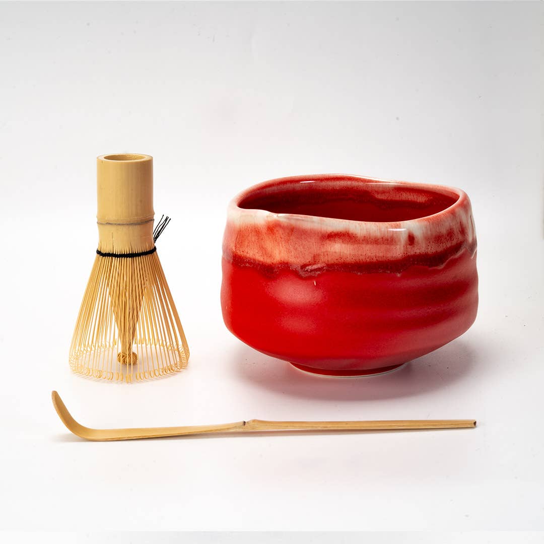 Red ceramic bowl with wooden whisk and spoon on a white background
