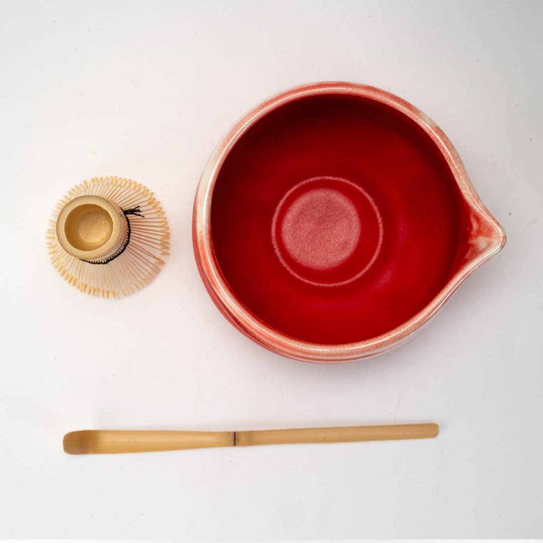 Red ceramic bowl with wooden scoop and whisk on a white background