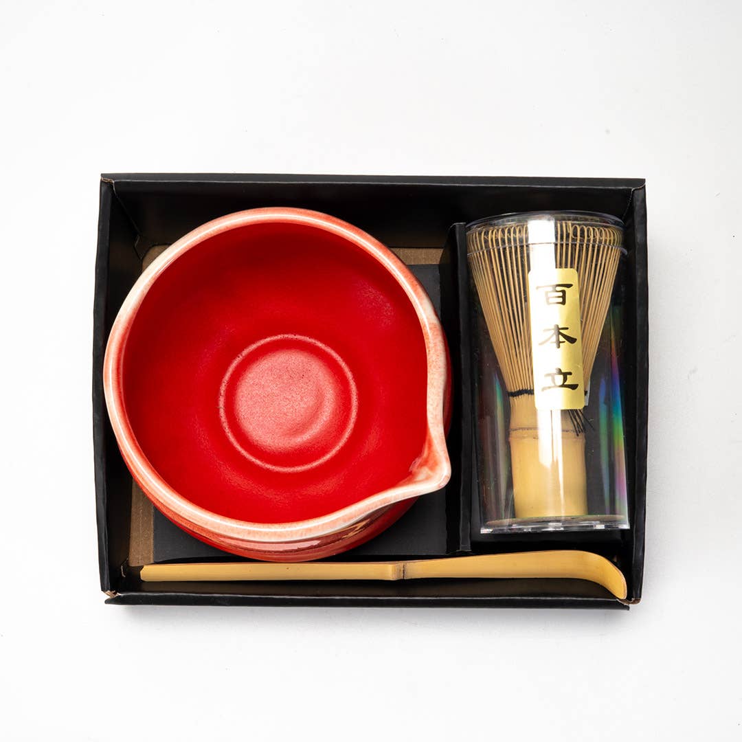 Tea set with a red bowl, gold whisk, and scoop in a black box on a white background