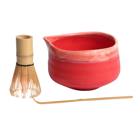 Red ceramic pitcher with wooden whisk and spoon on a white background